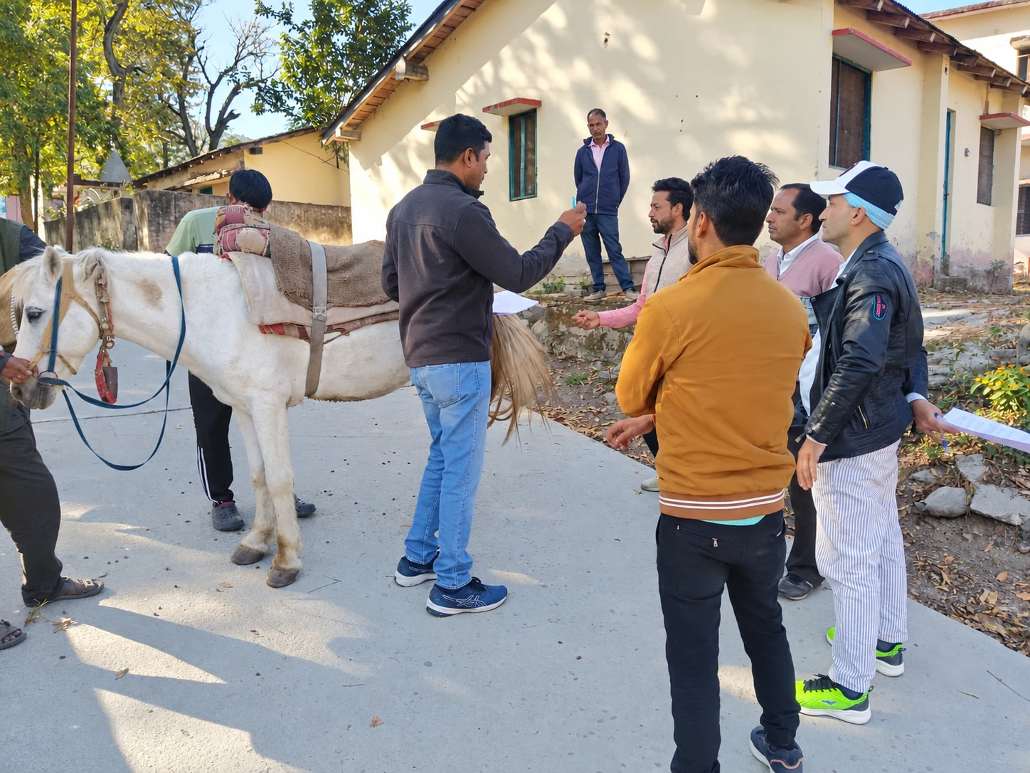A trainer explaining equine care to participants gathered beside a saddled horse
